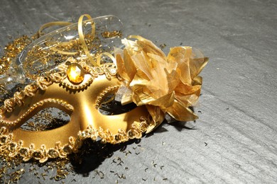 Photo of Beautiful golden carnival mask, glass and confetti on gray textured table, closeup