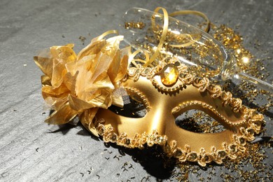 Beautiful golden carnival mask, glass and confetti on gray textured table, closeup