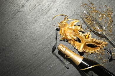 Photo of Beautiful golden carnival mask, bottle of sparkling wine, glass and confetti on gray textured table, flat lay. Space for text