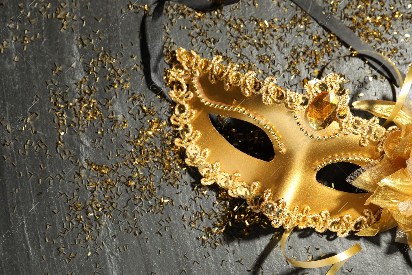 Photo of Beautiful golden carnival mask and confetti on gray textured table, top view. Space for text