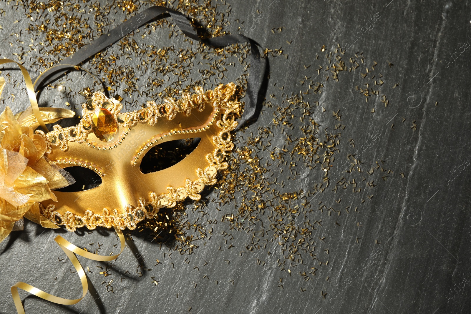 Photo of Beautiful golden carnival mask and confetti on gray textured table, top view. Space for text