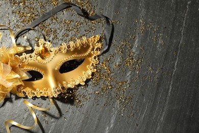 Beautiful golden carnival mask and confetti on gray textured table, top view. Space for text