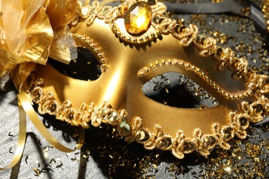 Photo of Beautiful golden carnival mask and confetti on gray textured table, closeup