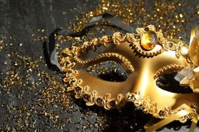 Beautiful golden carnival mask and confetti on gray textured table, closeup