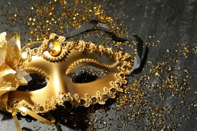 Photo of Beautiful golden carnival mask and confetti on gray textured table, top view