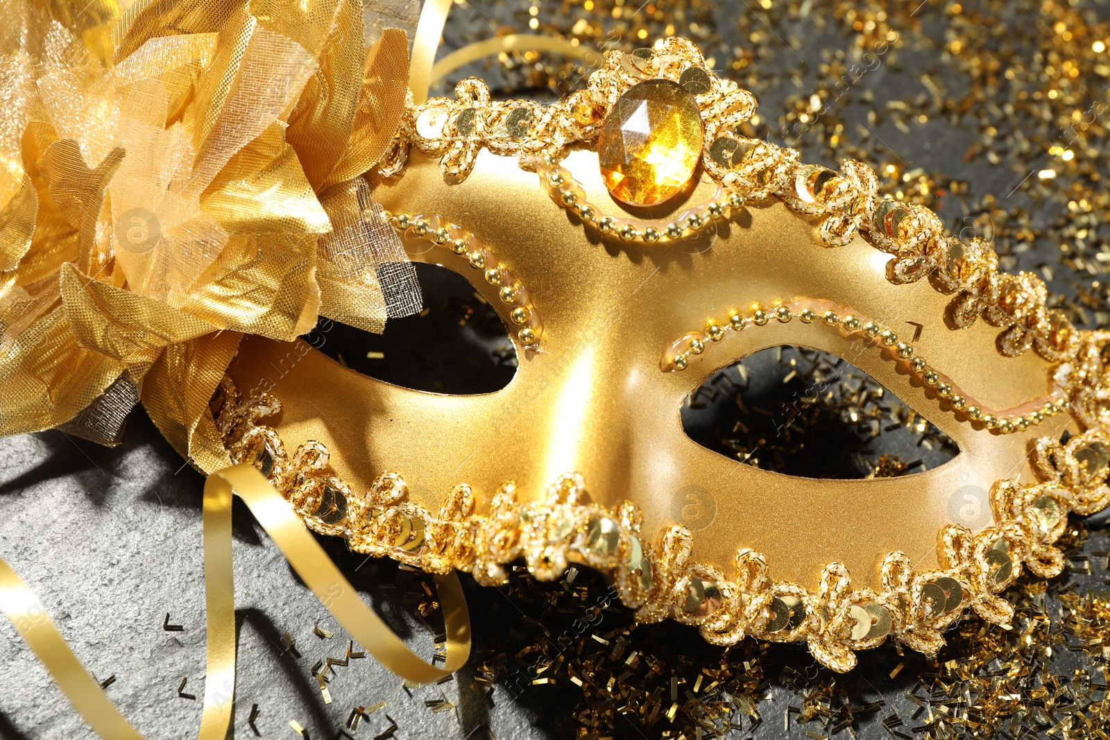 Photo of Beautiful golden carnival mask and confetti on gray textured table, top view