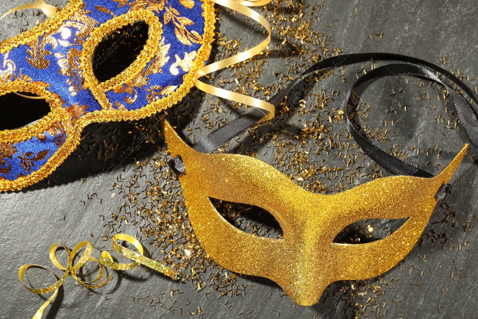 Photo of Beautiful carnival masks and confetti on gray textured table, flat lay