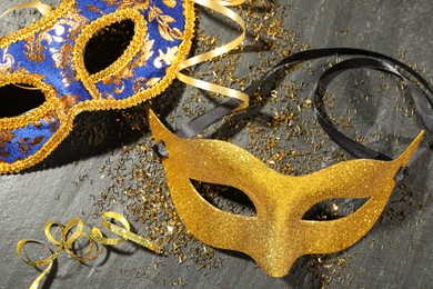 Beautiful carnival masks and confetti on gray textured table, flat lay