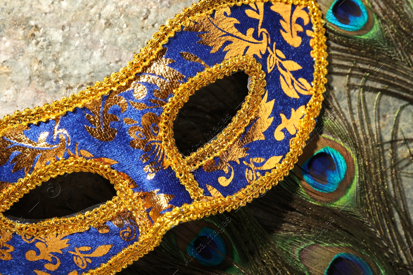 Photo of Beautiful bright carnival mask and peacock feathers on gray textured table, top view