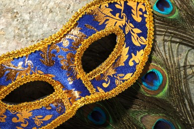 Beautiful bright carnival mask and peacock feathers on gray textured table, top view