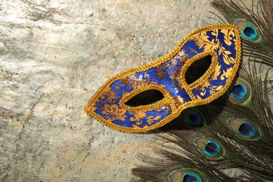 Beautiful bright carnival mask and peacock feathers on gray textured table, top view. Space for text