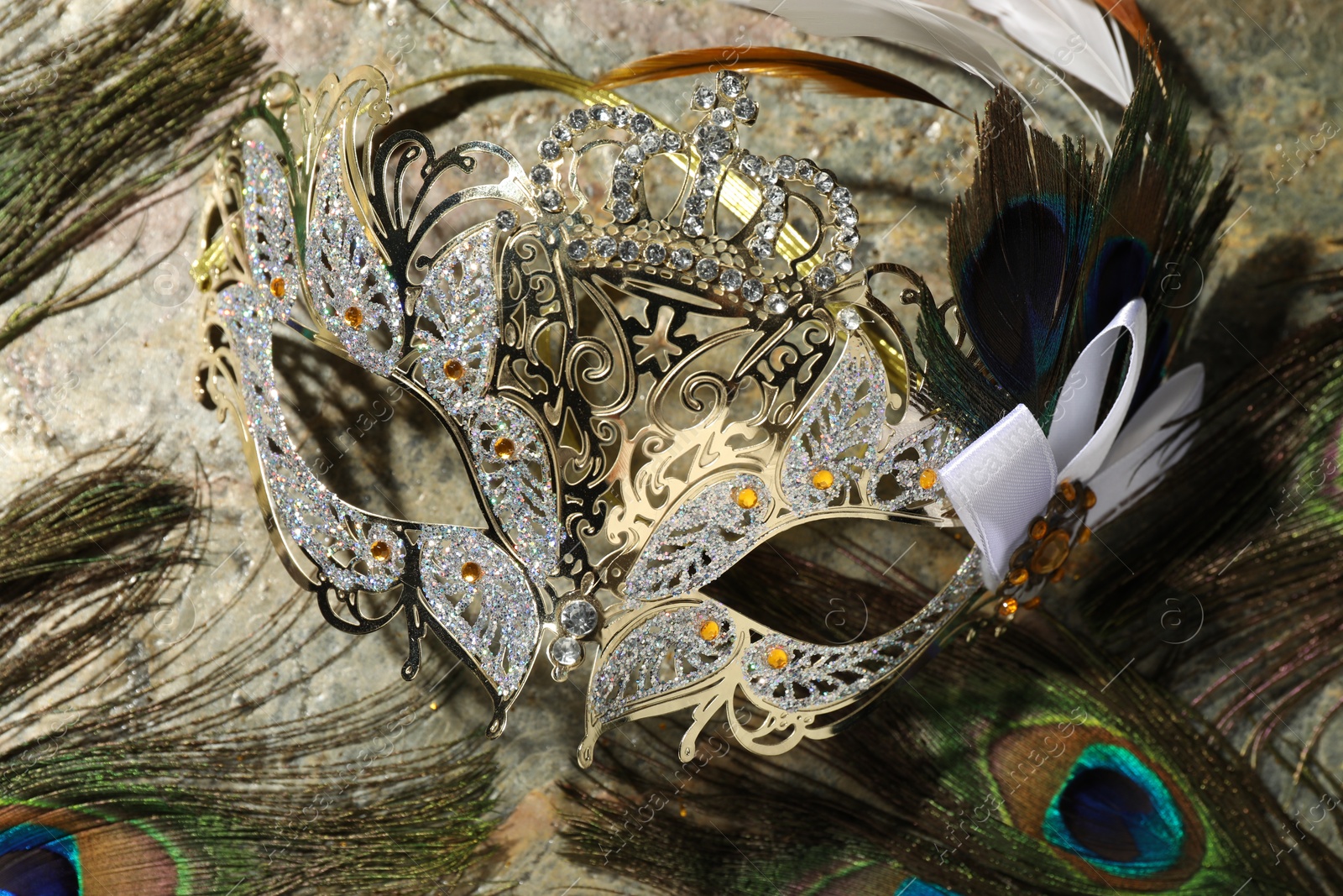 Photo of Beautiful bright carnival mask and peacock feathers on gray textured table, top view