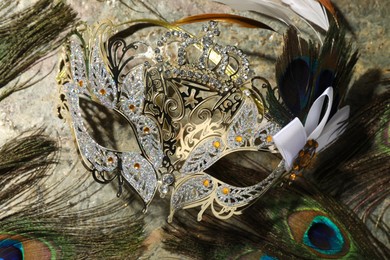 Beautiful bright carnival mask and peacock feathers on gray textured table, top view