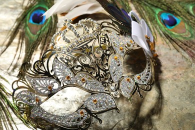 Photo of Beautiful bright carnival mask and peacock feathers on gray textured table, closeup