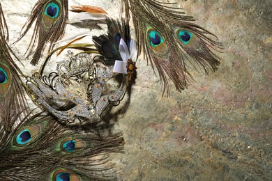 Beautiful bright carnival mask and peacock feathers on gray textured table, flat lay. Space for text