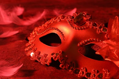 Beautiful carnival mask on table in red light, closeup