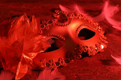 Photo of Beautiful carnival mask on table in red light, closeup