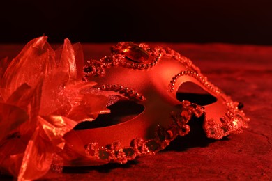 Photo of Beautiful carnival mask on table in red light, closeup