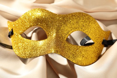 Photo of Beautiful golden carnival mask on beige fabric, top view