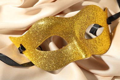 Photo of Beautiful golden carnival mask on beige fabric, top view