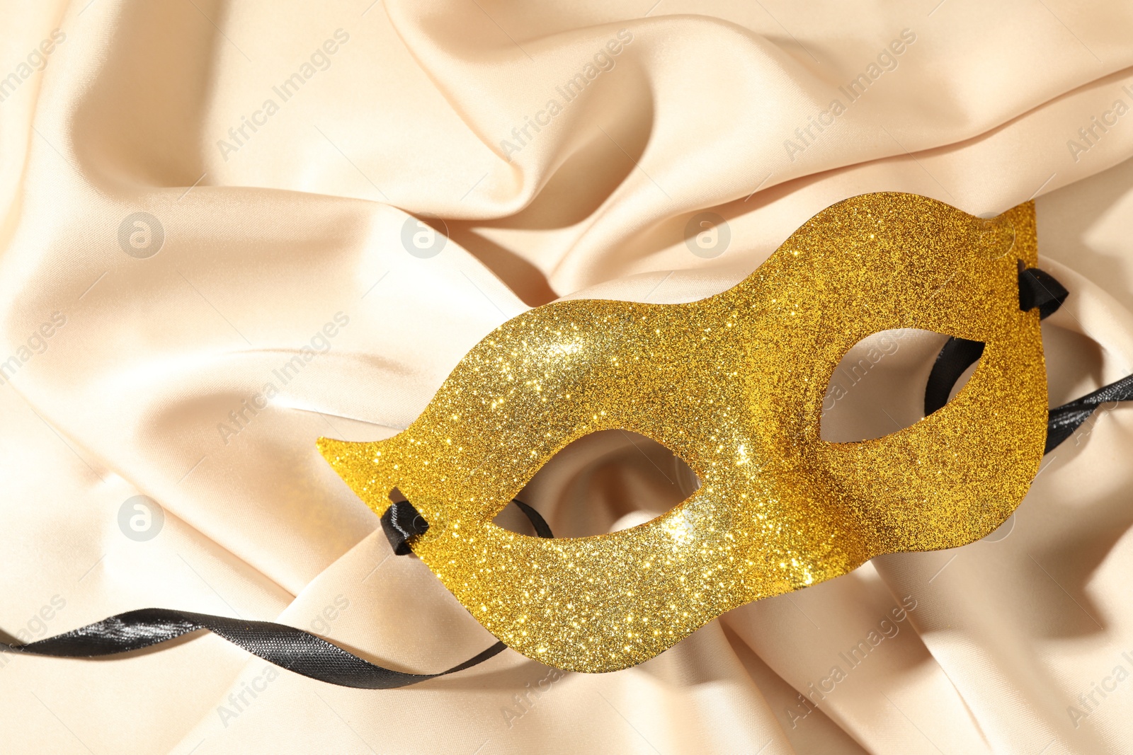 Photo of Beautiful golden carnival mask on beige fabric, top view