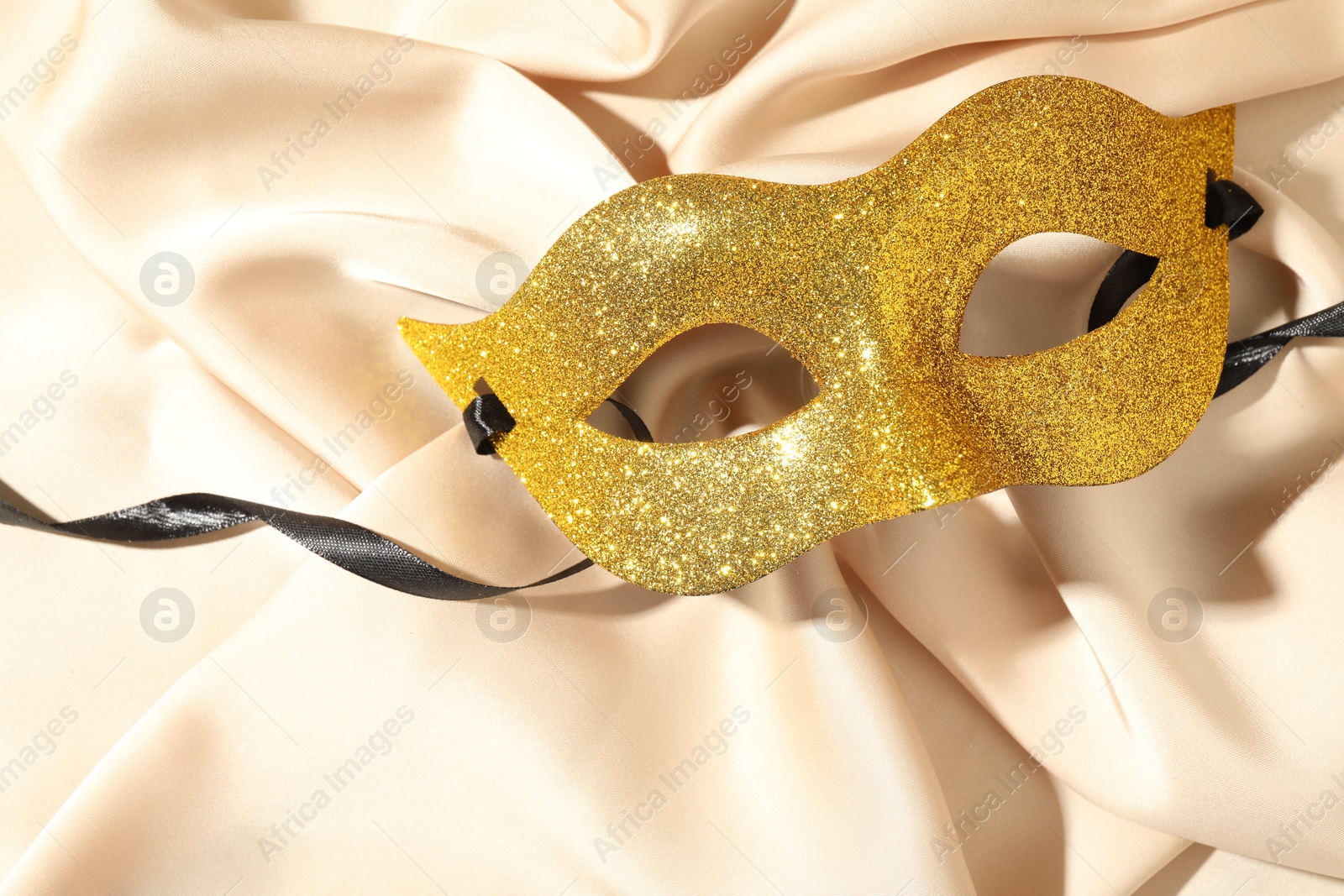 Photo of Beautiful golden carnival mask on beige fabric, top view