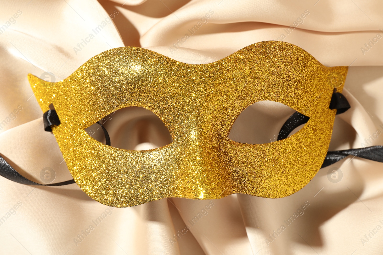 Photo of Beautiful golden carnival mask on beige fabric, top view