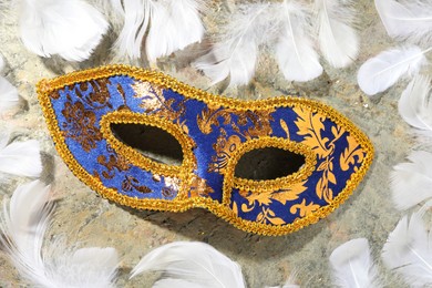 Beautiful bright carnival mask and white feathers on gray textured table, flat lay