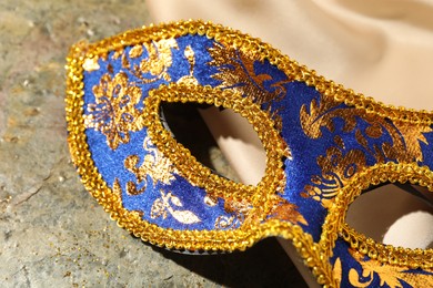 Beautiful bright carnival mask and beige fabric on gray textured table, closeup