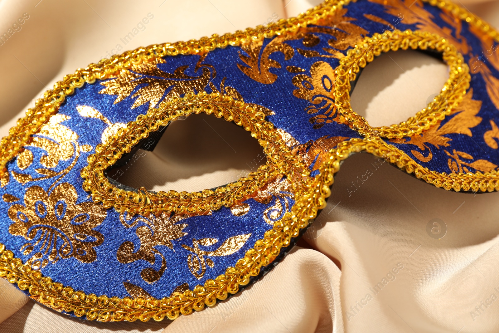 Photo of Beautiful bright carnival mask on beige fabric, closeup