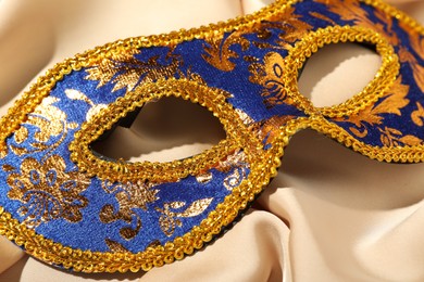 Photo of Beautiful bright carnival mask on beige fabric, closeup