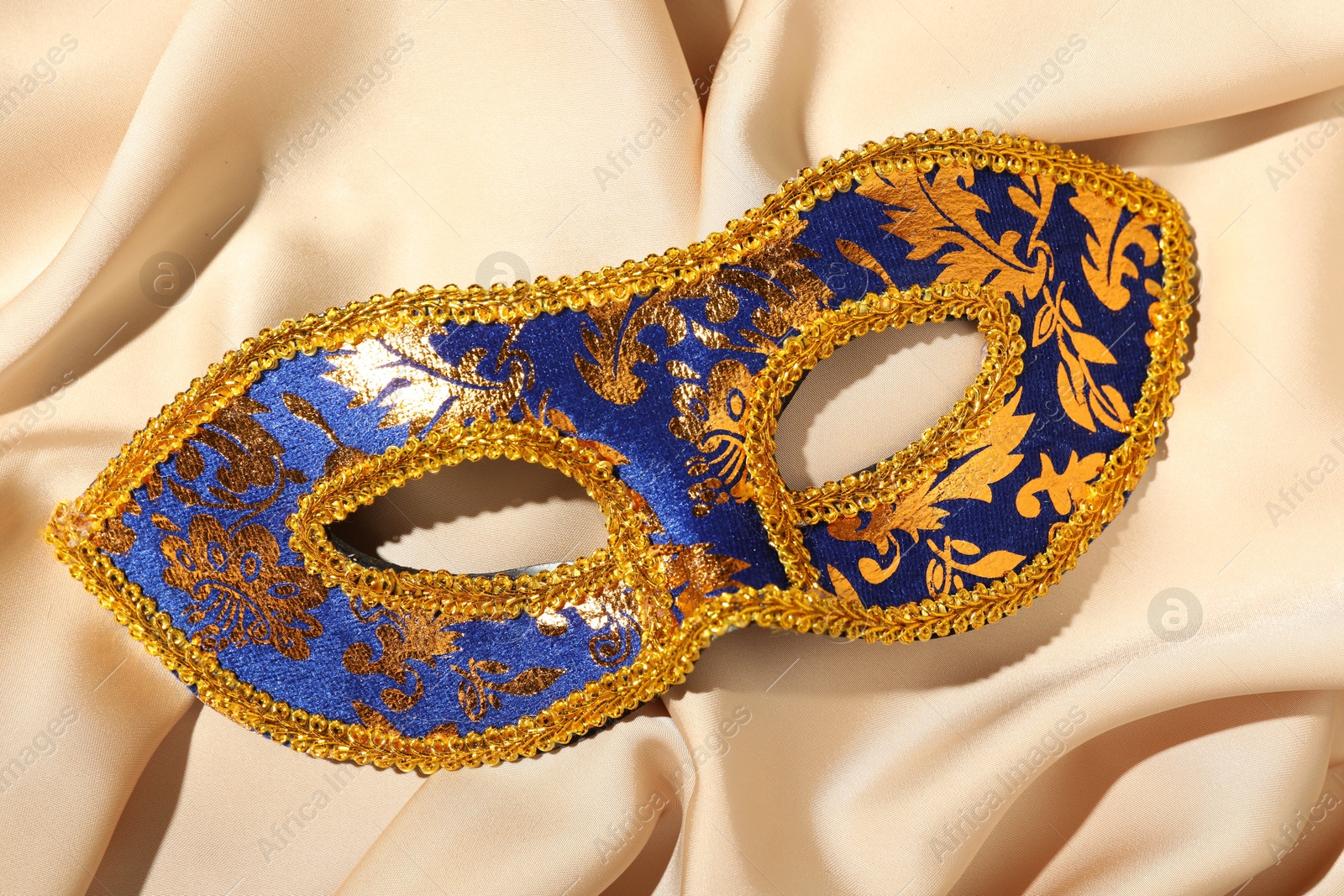 Photo of Beautiful bright carnival mask on beige fabric, top view