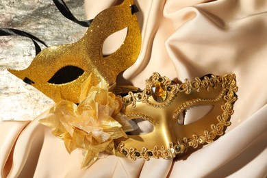 Photo of Beautiful golden carnival masks and beige fabric on table, top view