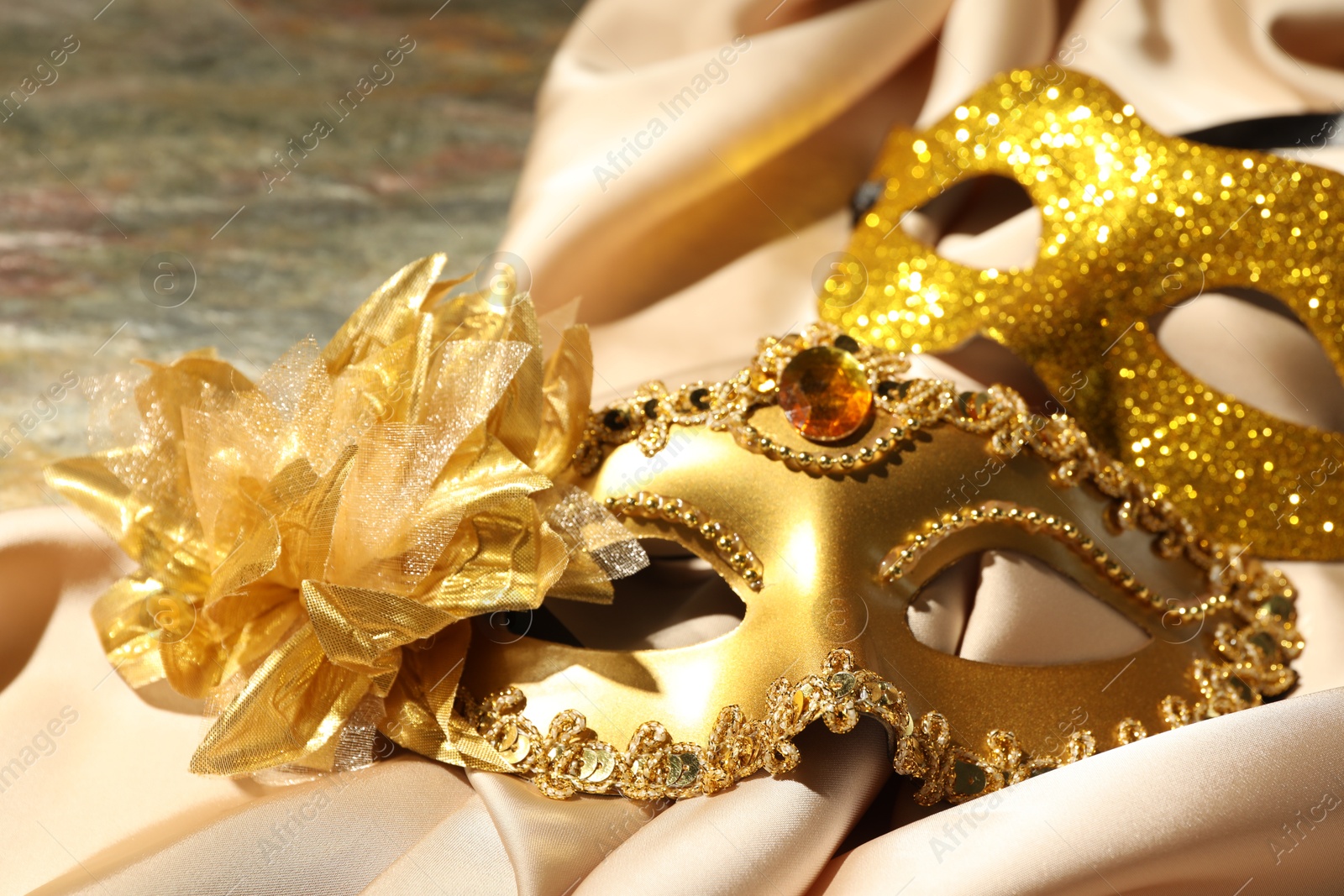 Photo of Beautiful golden carnival masks and beige fabric on table, closeup