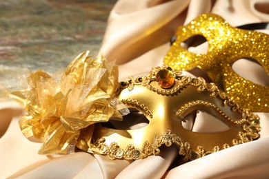 Photo of Beautiful golden carnival masks and beige fabric on table, closeup