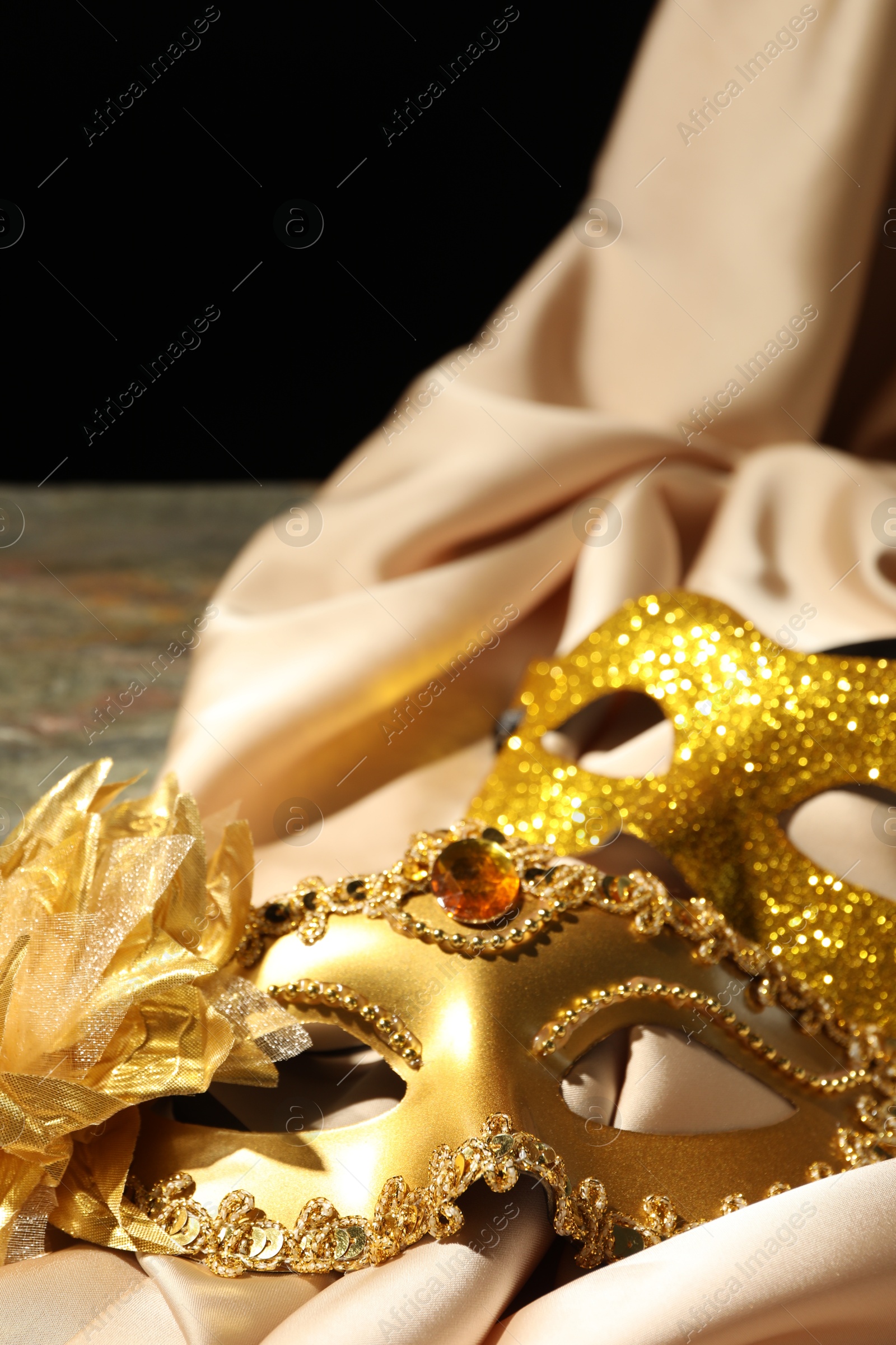 Photo of Beautiful golden carnival masks and beige fabric on table, closeup