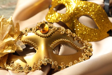 Photo of Beautiful golden carnival masks and beige fabric on table, closeup