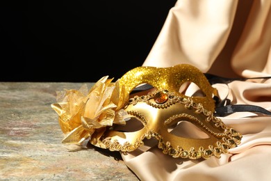 Beautiful golden carnival masks and beige fabric on gray textured table against black background