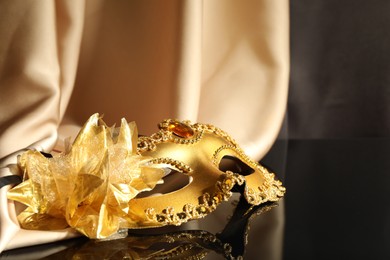 Photo of Beautiful golden carnival mask and beige fabric on black mirror surface