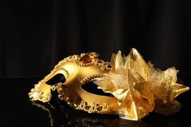 Photo of Beautiful golden carnival mask on black mirror surface