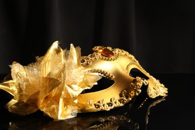 Photo of Beautiful golden carnival mask on black mirror surface