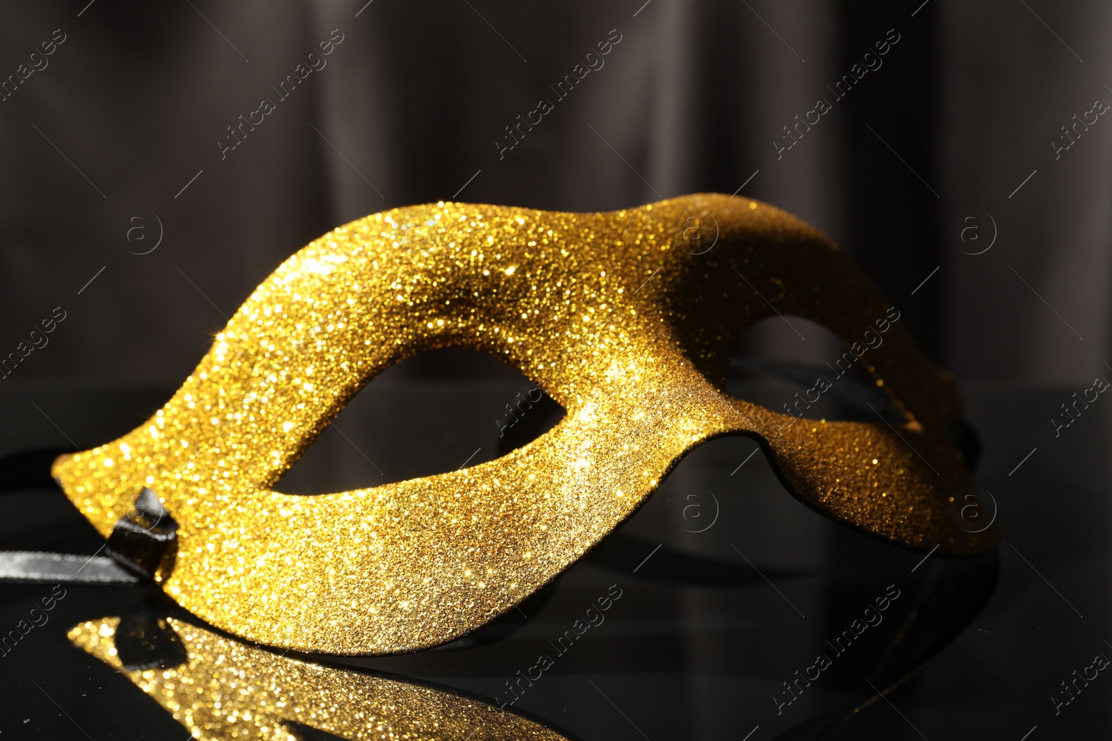 Photo of Beautiful golden carnival mask on black mirror surface, closeup