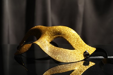 Photo of Beautiful golden carnival mask on black mirror surface