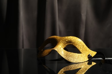 Photo of Beautiful golden carnival mask on black mirror surface