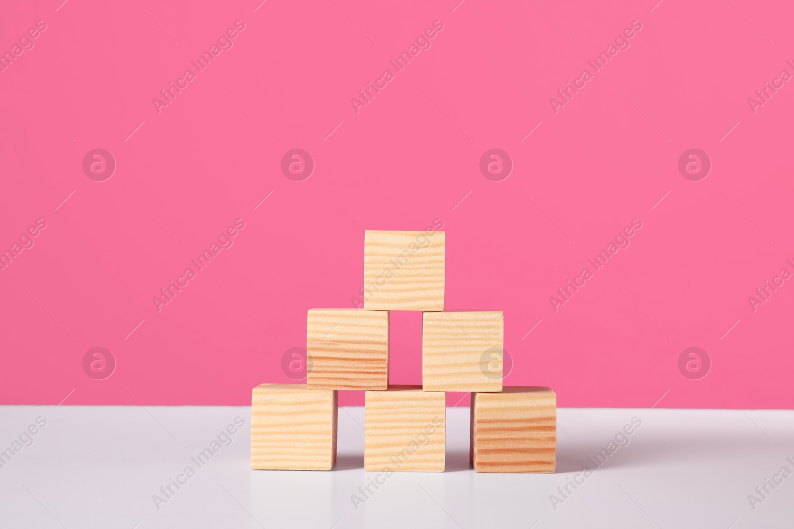 Photo of Many wooden cubes on white table against pink background