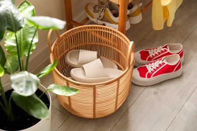 Photo of Basket with slippers for guests and sneakers in entryway at home