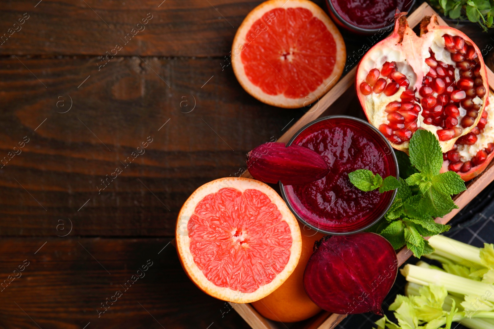 Photo of Glass of tasty beetroot smoothie, fresh vegetables, fruits and mint in box on wooden table, top view with space for text. Vegan drink