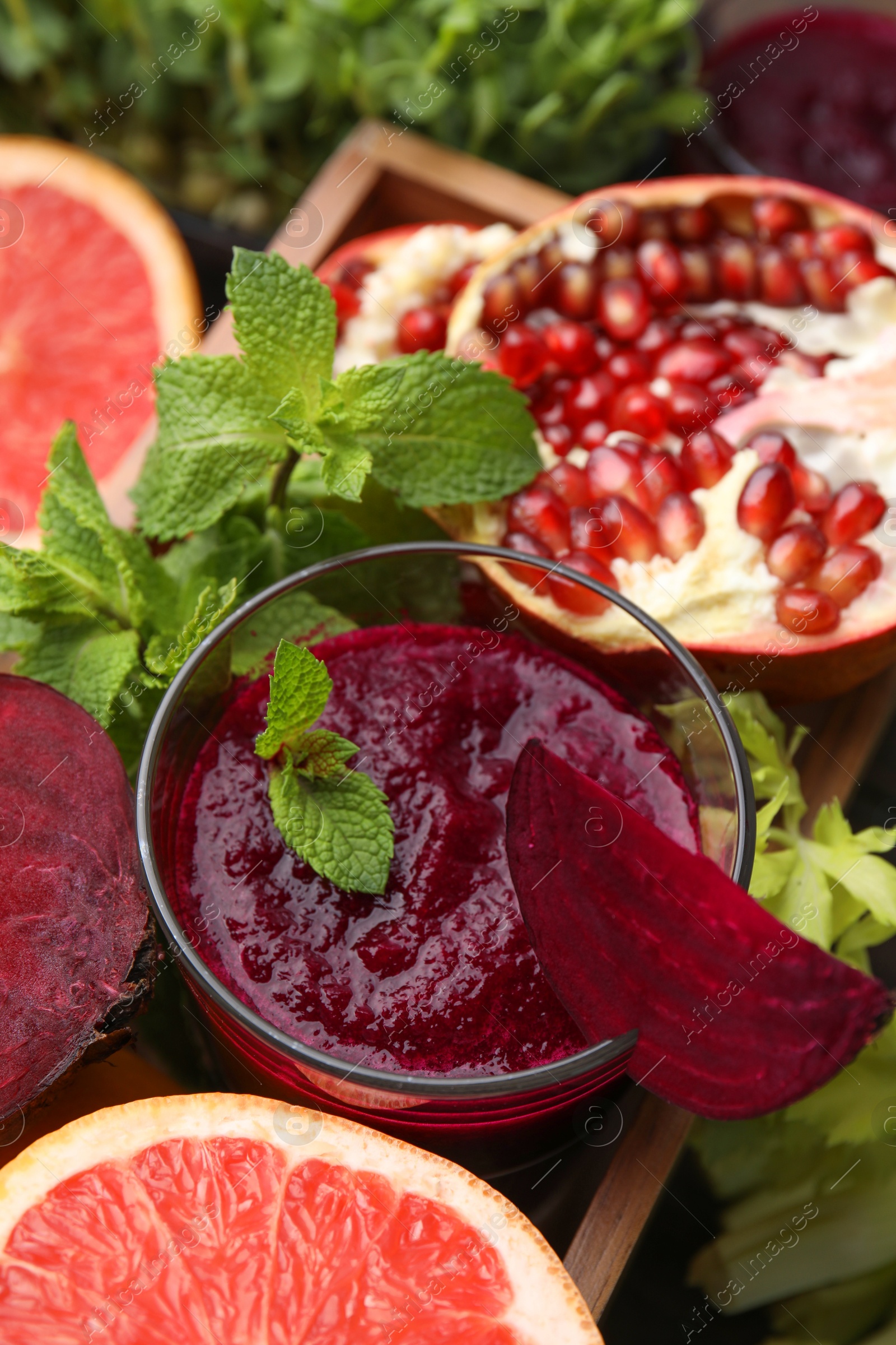 Photo of Tasty beetroot smoothie with mint in glass, fresh vegetables and fruits on table, closeup. Vegan drink