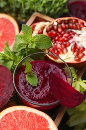 Tasty beetroot smoothie with mint in glass, fresh vegetables and fruits on table, closeup. Vegan drink