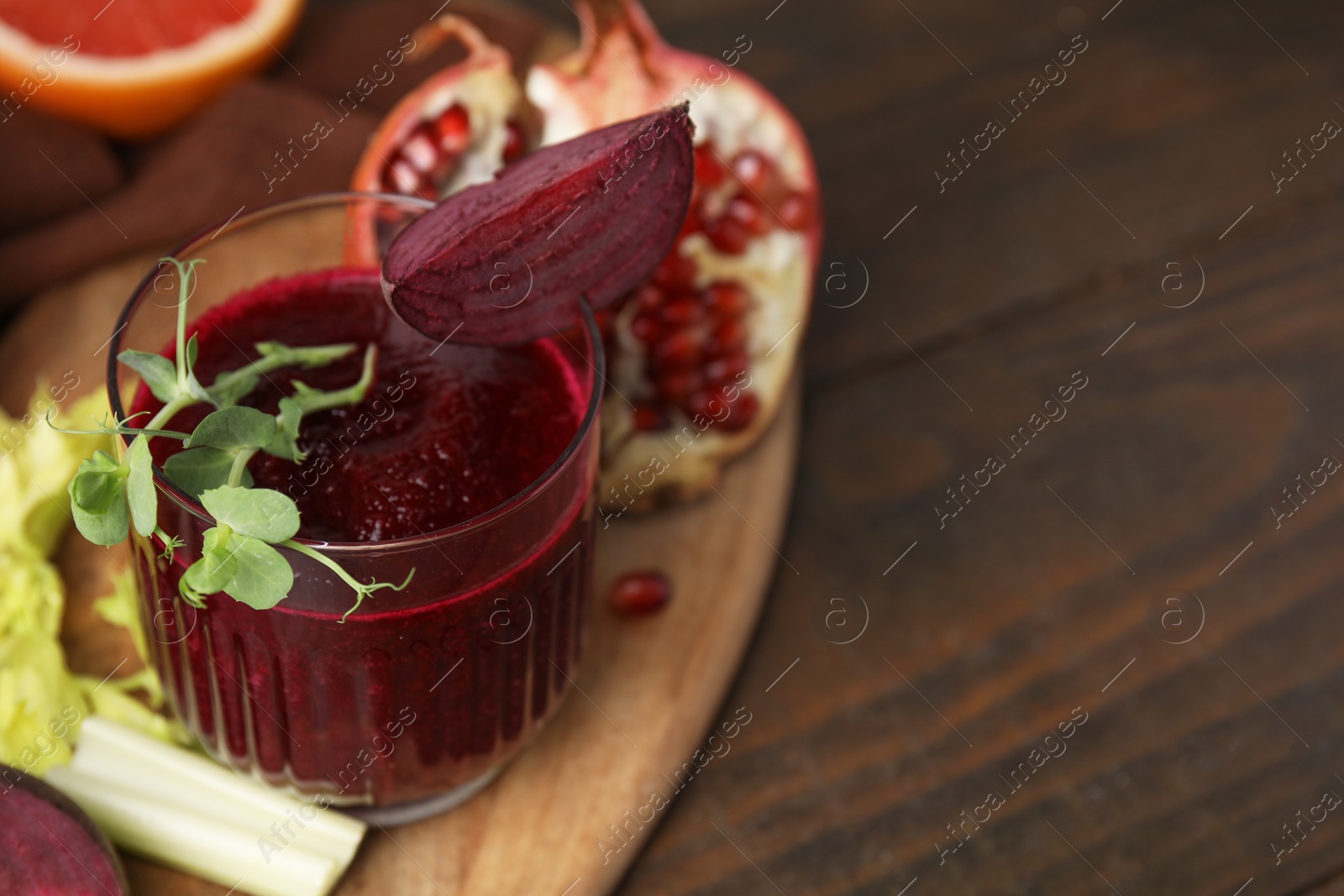 Photo of Tasty beetroot smoothie with microgreens in glass, fresh vegetables and fruits on wooden table, closeup. Vegan drink